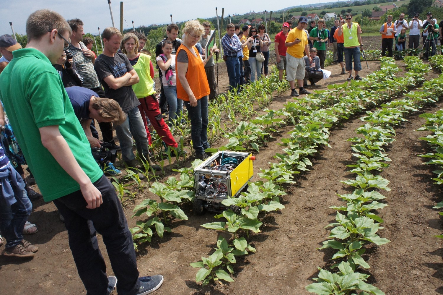 Foto von einem der Tasks. Kamaro 2010 fährt durch eine Feldreihe. Ein Kamaro steht am Anfang der Reihe und beobachtet. Die Jury steht links vom Roboter am Feldrand. Dahinter und um das Feld sammeln sich einige Zuschauer