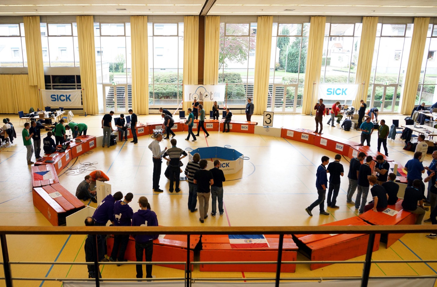 Bild von oben auf die Arena. Die Arena ist in der örtlichen Sporthalle aus Biertischen aufgebaut. Sie ist Donut förmig und aktuell stehen enige Leute in und um die Arena