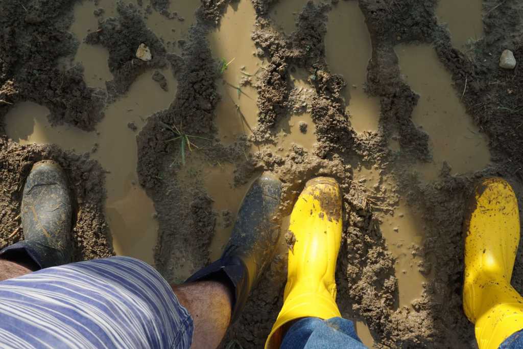Zwei Füße in Gummistiefeln stehen mehrere Zentimeter im Schlamm